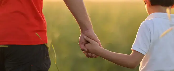 Young father holding his son’s hand while walking in the grass