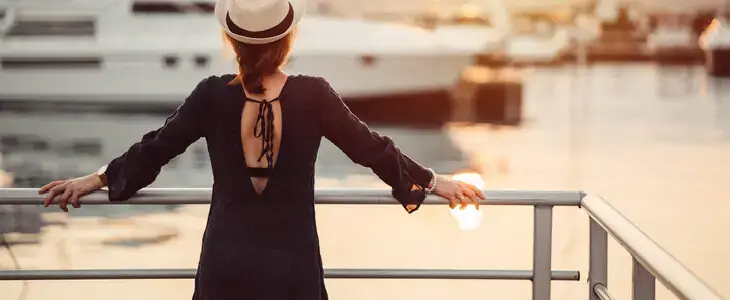 A wealthy woman looking standing on a deck and looking at her yacht